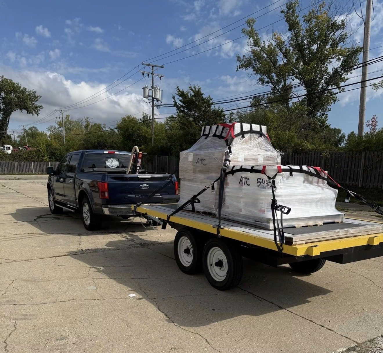 Navy Ford F-150 towing an ATC Supply flatbed trailer loaded with a shrink-wrapped and strapped pallet of coating materials labeled ATC 543, ready for jobsite delivery