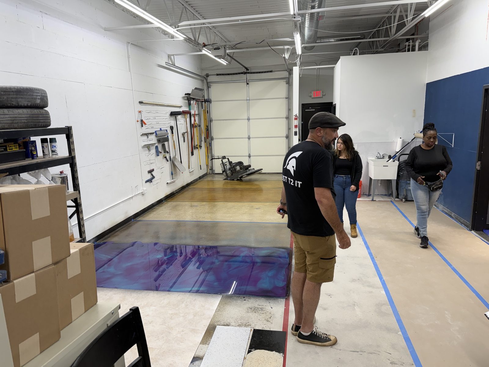 Instructor and students in the ATC Supply hands-on demo bay watching a purple metallic epoxy pour cure on the floor with the tool wall in the background