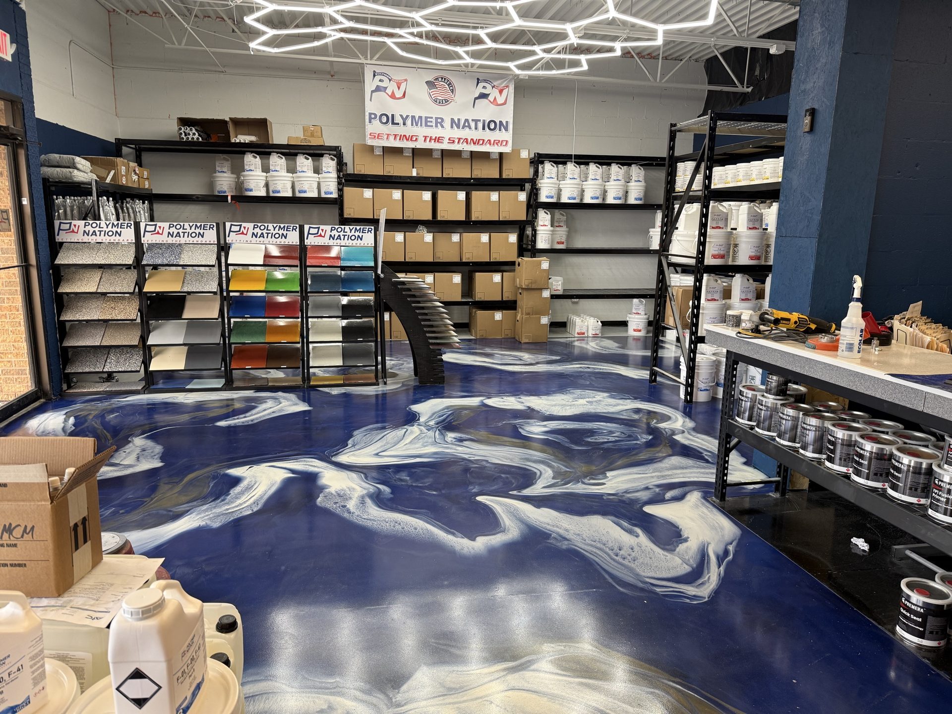 ATC Supply showroom in Merrillville, Indiana featuring a dramatic navy metallic epoxy floor with white and gold swirls, Polymer Nation sample racks, and hex ceiling lighting