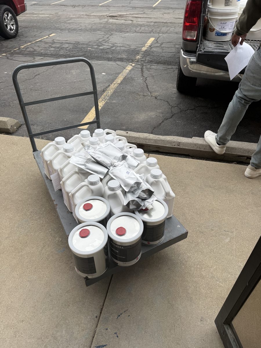 A cart of Premera concrete polishing cans, hardener jugs, and polyaspartic pouches staged on the ATC Supply sidewalk for a customer pickup, with the contractor's SUV backed up to the door