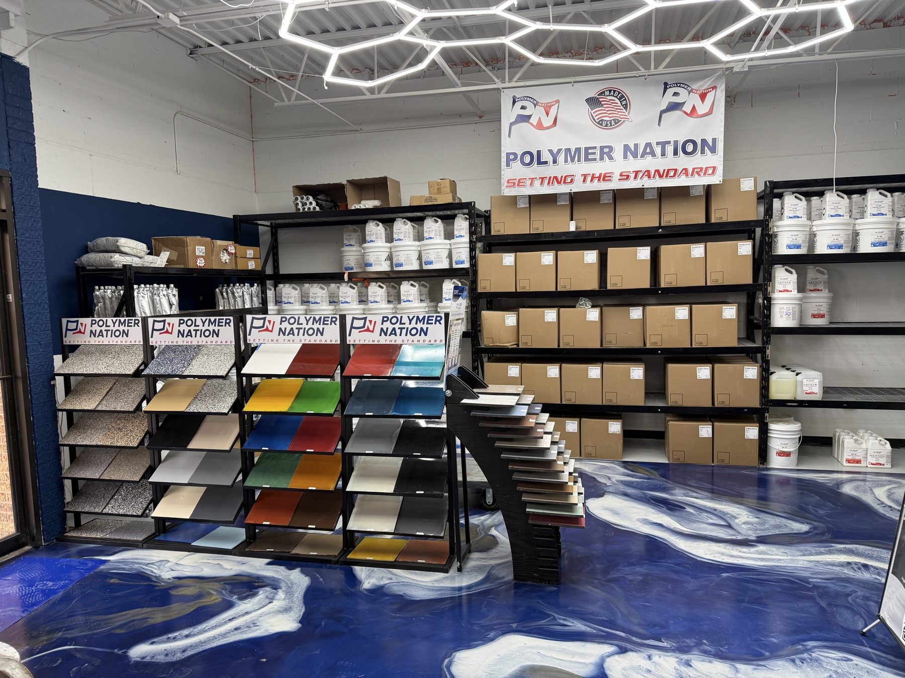 ATC Supply showroom sample racks displaying dozens of solid color and flake finish sample boards under branded Polymer Nation signage, over the store's signature navy metallic epoxy floor