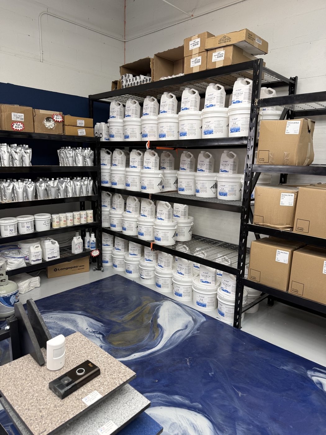 Polymer Nation white jug wall with F-41 topcoat containers, silver polyaspartic pouches, and flake box shelving stocked deep for immediate pickup