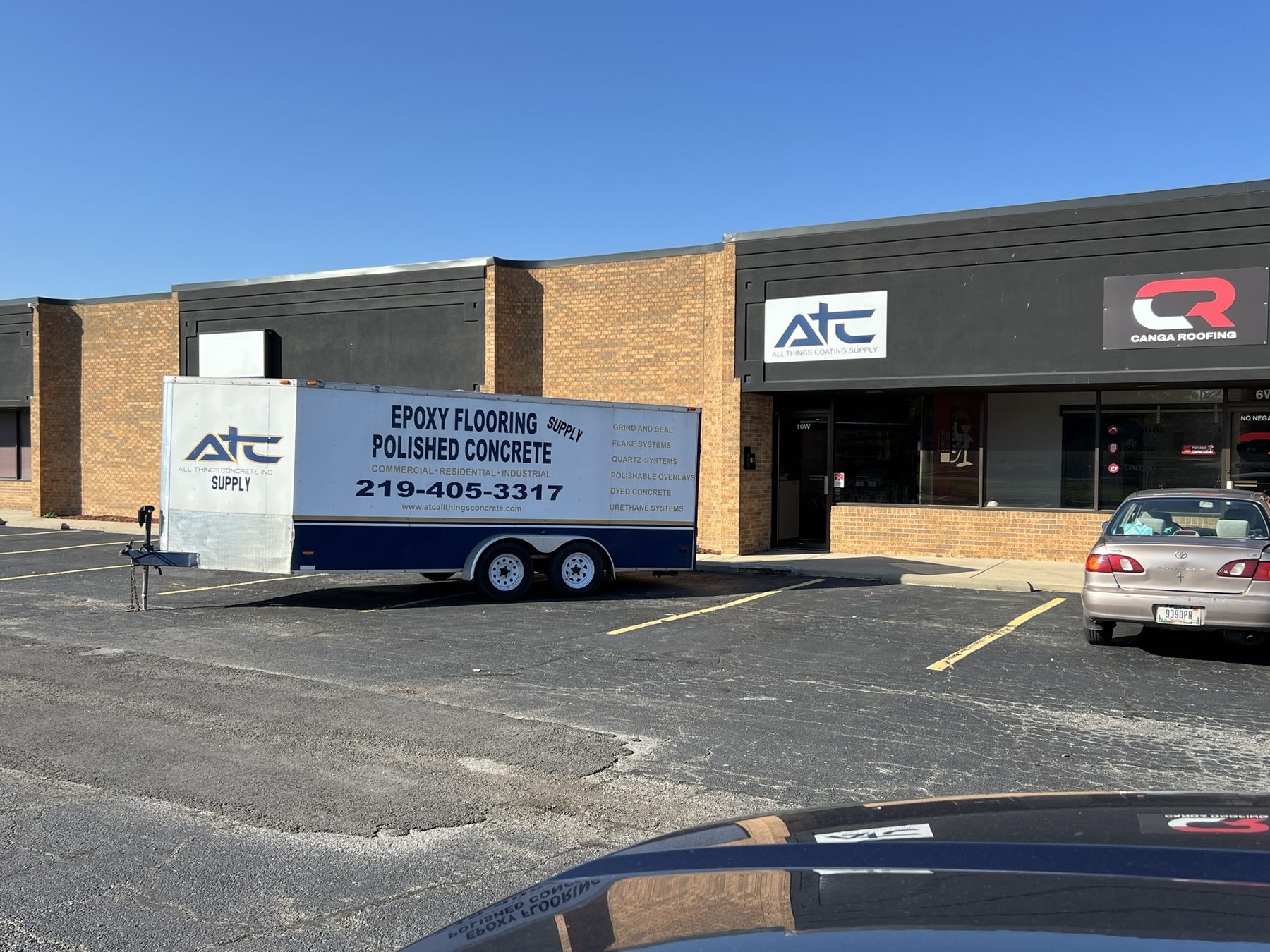 The ATC Supply storefront in Merrillville, Indiana with the retired ATC install trailer parked out front, branded with the systems the founder used to install: grind and seal, flake systems, quartz, polishable overlays, dyed concrete, and urethane