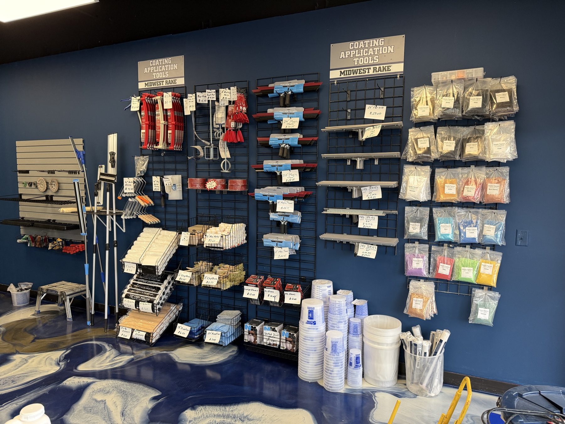 ATC Supply application tools wall stocked with Midwest Rake gauge rakes, feather trowels, chip brushes, mixing cups, mixing paddles, and a full pigment and flake color rack in labeled bags